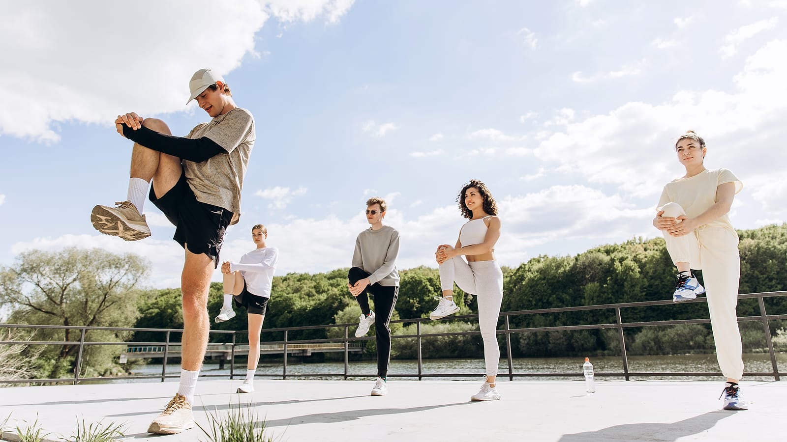Fünf Personen wärmen sich beim Small Group Training draußen am Wasser auf